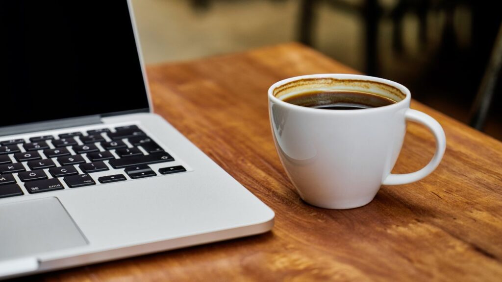 Obrazek przedstawia laptop i postawioną obok niego kawę