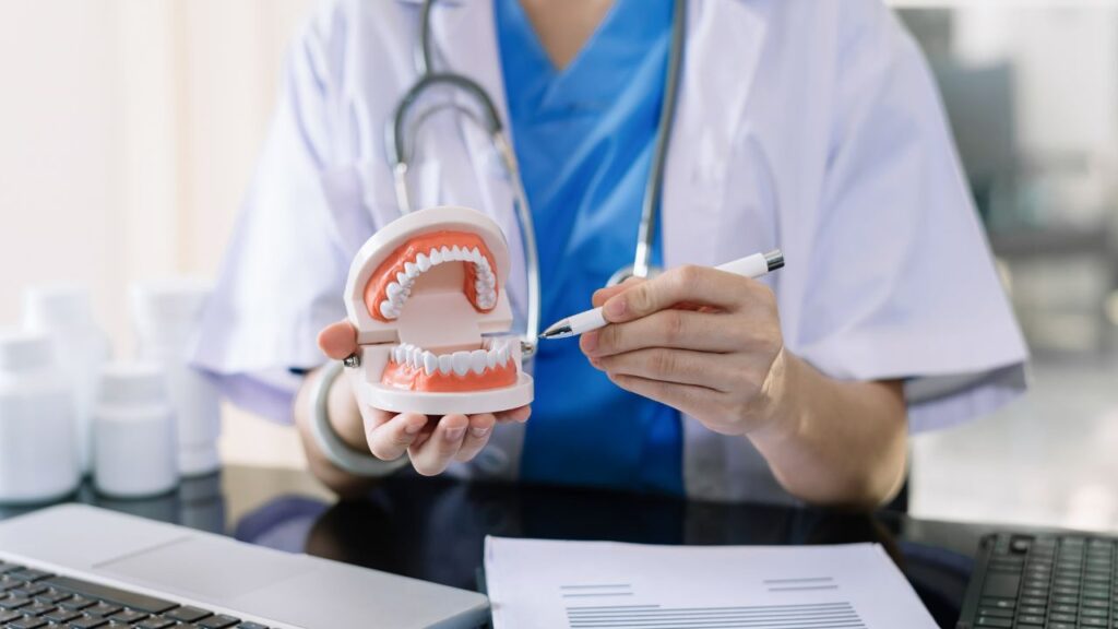 Obrazek przedstawia stomatolog, która pokazuje coś na makiecie szczęki